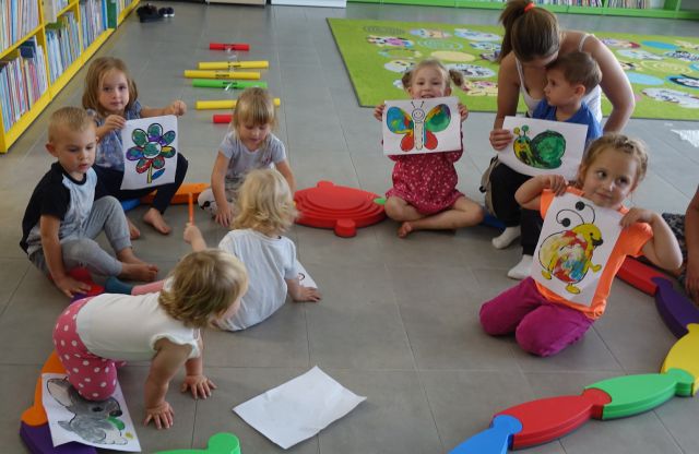 dzieci siedzą na podłodze i pozują do zdjęcia z wykonanymi przez siebie wyklejankami