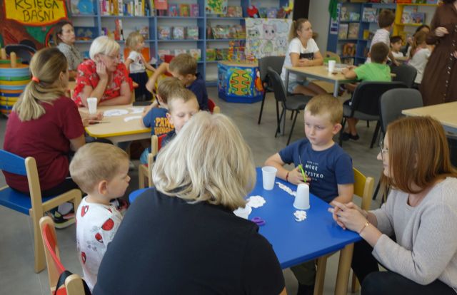 dzieci i opiekunowie siedzą przy stolikach 