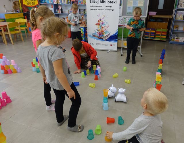 dzieci sterują robotami, które jeżdżą pomiędzy ułożonymi kolorowymi kubeczkami