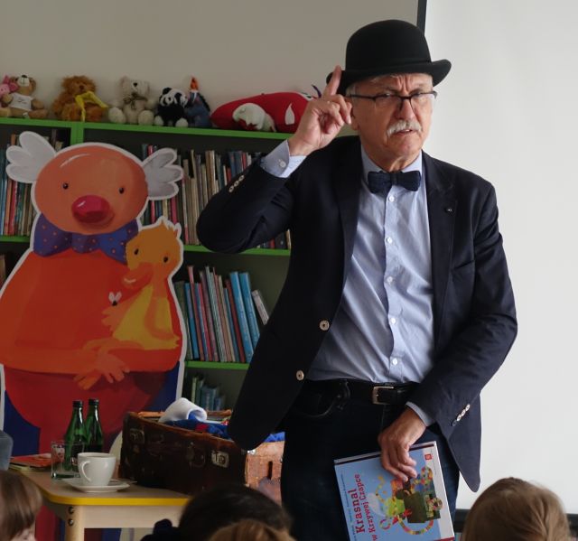 mężczyzna w meloniku stoi, obok niego baner z bohaterem jego książki - panem Kuleczką