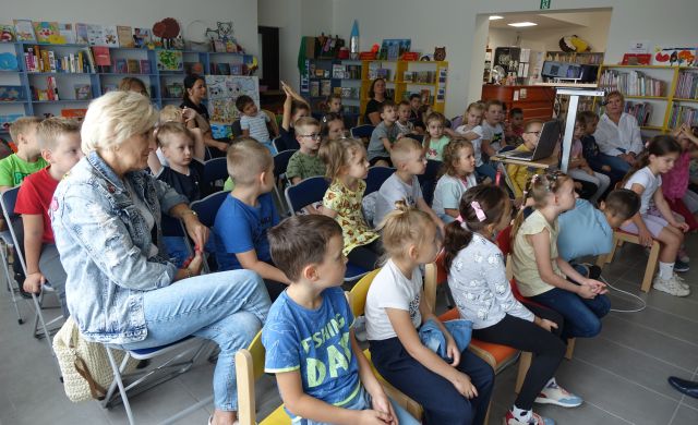 około 50 dzieci siedzi na krzesełkach, w tle regały