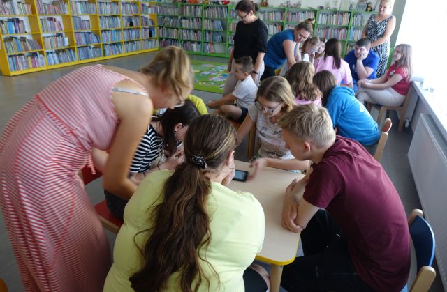 młodzież siedzi przy stolikach i steruje robotami Photon przy użyciu tabletów