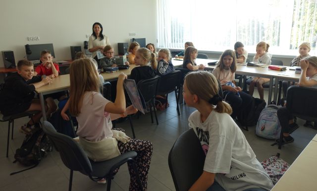 dziewczyna pokazują koleżankom i kolegom siedzącym przy stołach komiks