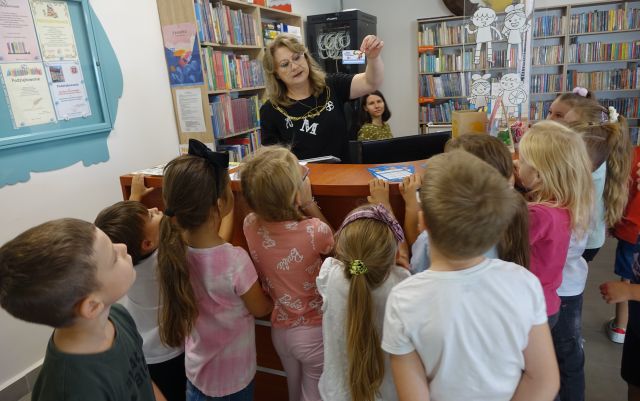 bibliotekarka pokazuje przedszkolakom kartę małego czytelnika