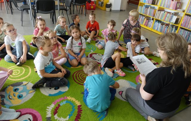 bibliotekarka czyta siedzącym na kolorowym dywanie książkę