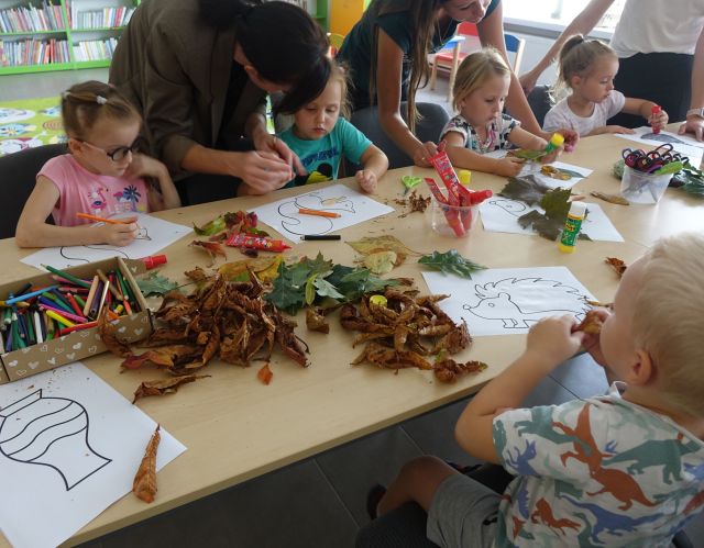 dziecie siedzą przy stole i wyklejają kompozycje z kolorowych liści
