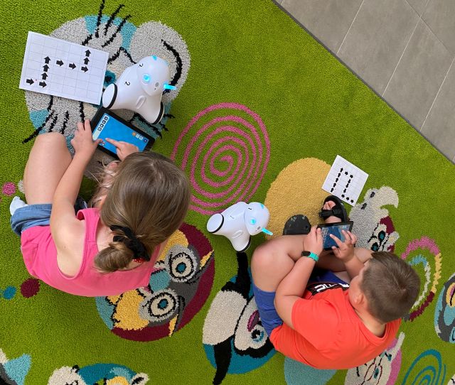 chłopiec i dziewczynka siedzą na kolorowym dywanie i sterują robotami