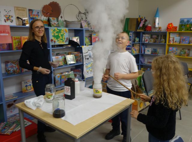 dwóch chłopców patrzy na ulatniającą się parę, obok stoi kobieta, w tle regały