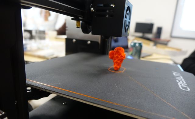 drukarka 3D drukuje pomarańczową figurkę