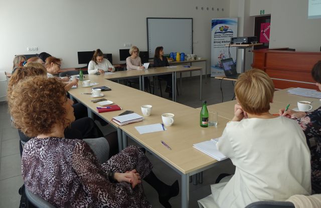 osoby dorosłe siedzą przy stołąch, na których leżą kartki i filiżanki, sala komputerowa