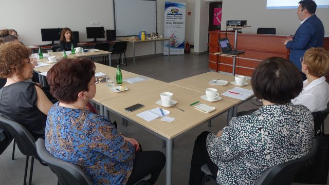 osoby dorosłe siedzą przy stołąch, na których leżą kartki i filiżanki, sala komputerowa