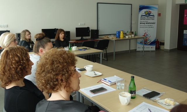 osoby dorosłe siedzą przy stołąch, na których leżą kartki i filiżanki, sala komputerowa