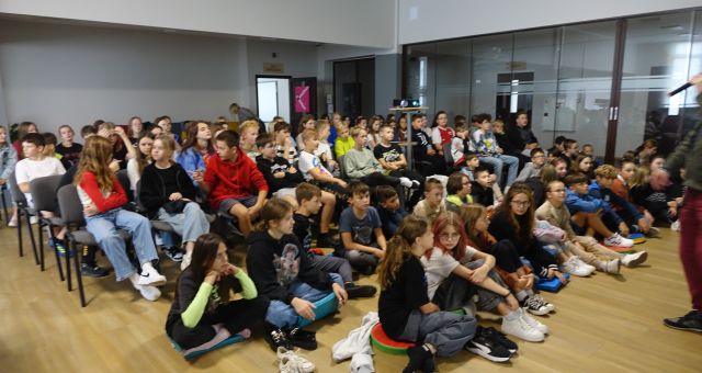 młodzie z klas V i VI siedzi na podłodze i na krzesłach