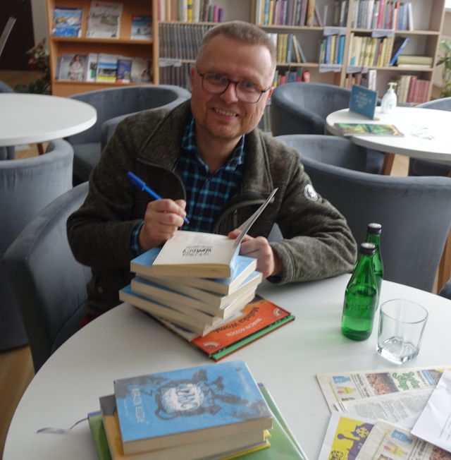 pisarz wpisuje się w książki jego autorstwa z biblioteki, siedząc przy białym stoliku