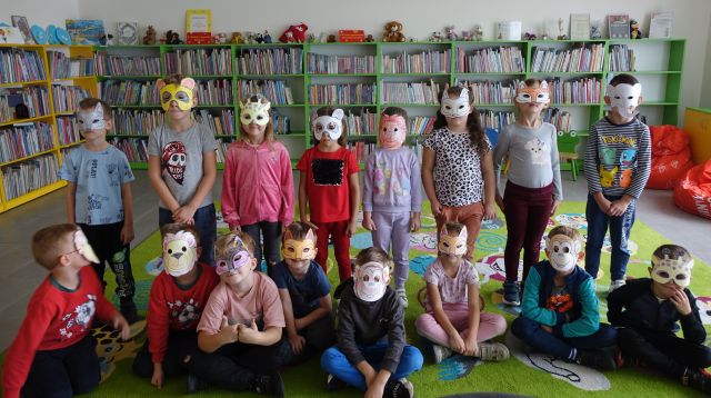 przedszkolaki pozują do zdjęcia w wykonanych przez siebie maskach zwierząt, w tle regały z książkami