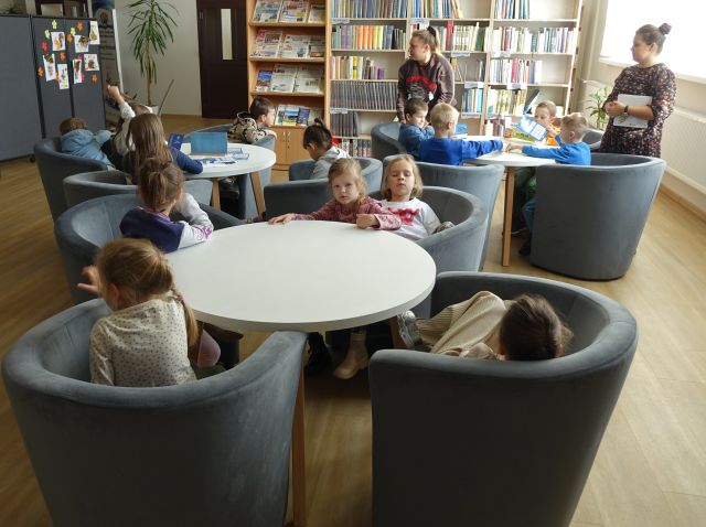 Przedszkolaki siedzą na siwych fotelach w czytelni biblioteki