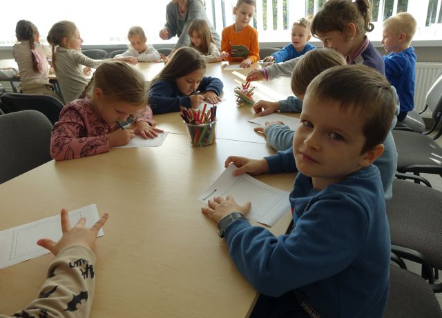 przedszkolaki siedzą przy stolikach i malują
