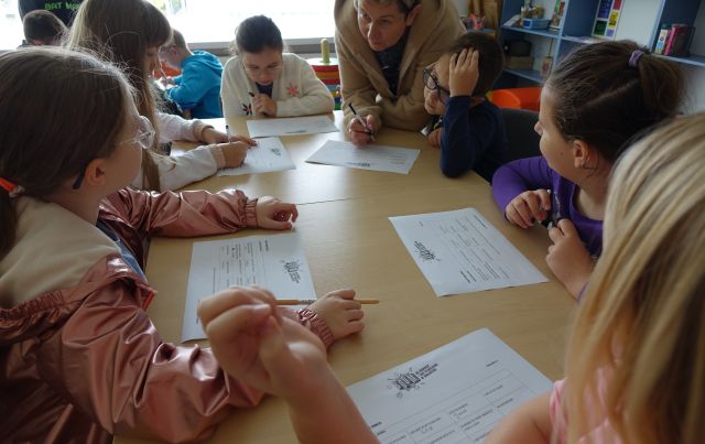 dzieci siedzą przy stolikach i rozwiązują bingo