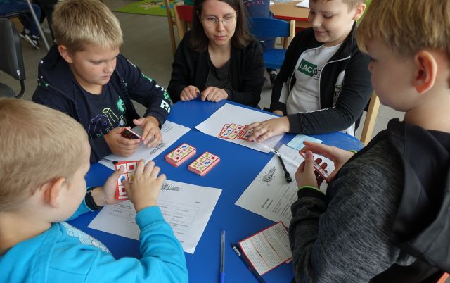 dzieci siedzące przy stolikach grają w grę planszową