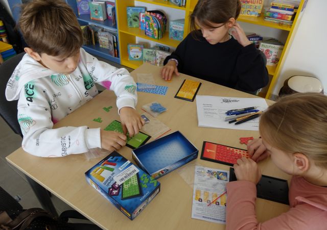 dzieci siedzące przy stolikach grają w grę planszową