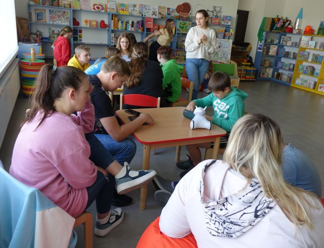 młodzież siedzi przy stolikach i steruje robotami Photon przy pomocy tabletów