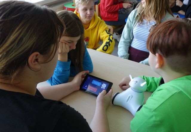 młodzież siedzi przy stolikach i steruje robotami Photon przy pomocy tabletów