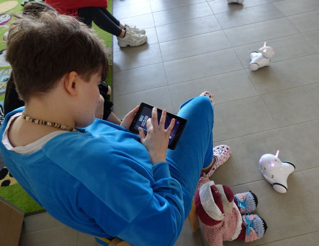 dziewczyna siedzi na podłodze i steruje robotem Photon przy pomocy tabletów