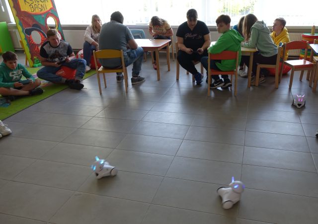 młodzież siedzi przy stolikach i steruje robotami Photon przy pomocy tabletów