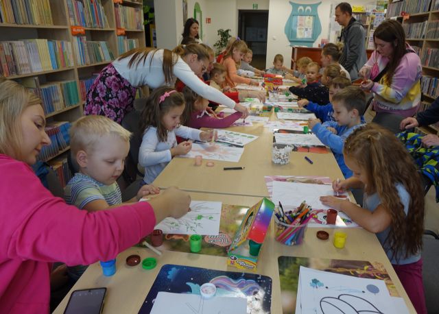 dzieci i opiekunowie wykonują prace plastyczne siedząc przy stołach