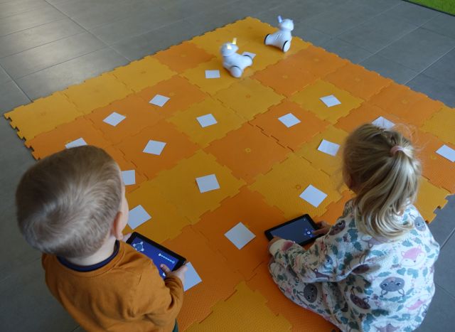 dzieci sterują przy użyciu tabletów robotami Photon jeżdżącymi po pomarańczowej macie