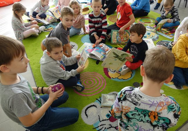 przedszkolaki na kolorowym dywanie przeglądają książki