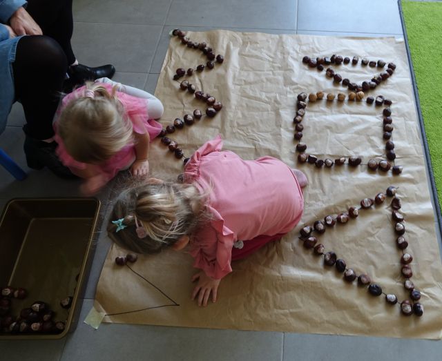 dwie małę dziewczynki w różowych bluzkach układają na podłodze kasztany