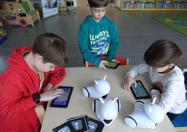 dwóch chłopców i dziewczynka sterują robotami Photon przy użyciu tabletów