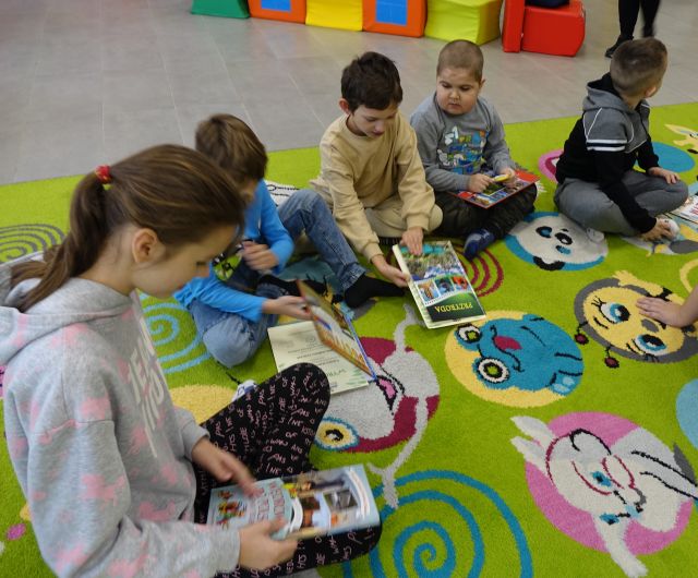 dziecisiedzą na klolorowym dywanie i przeglądają książki