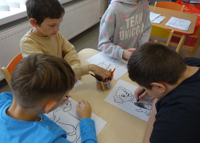 4 dzieci siedzi przy stole i maluje psy