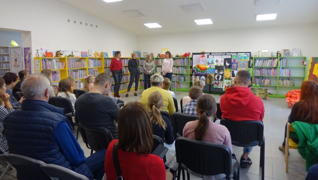 uroczystość wręczenia nagró w konkursie, 4 osoby dorosłe stoją przed siedzącymi dziećmi z opiekunami, w tle regały z książkami