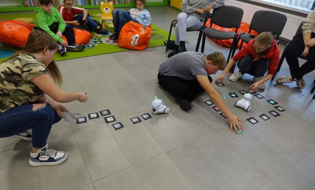 młodzież struje robotami Photon przy użyciu tabletów, roboty jeżdżą po podłodze pomiędzy strzałkami