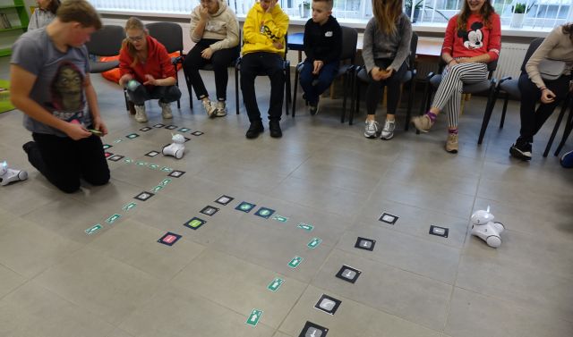 młodzież struje robotami Photon przy użyciu tabletów, roboty jeżdżą po podłodze pomiędzy strzałkami
