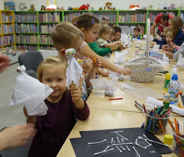 dziewczynka pokazuje wykonane przez siebie duszki, w tle pracujące dzieci i rodzice