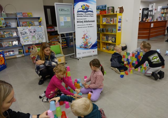 dzieci siedzą na podłodze i ukłądają kolorowe kubeczki