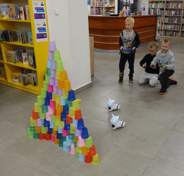 dzieci sterują robotami Photon, prezd nimi stoją ułożone w piramidę kolorowe kubeczki