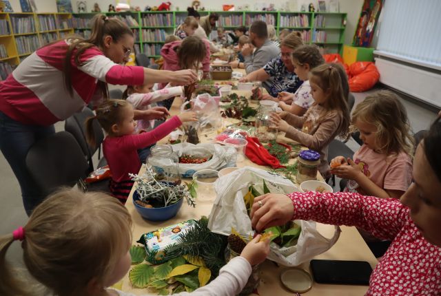 dzieci i rodzice siedzą przy stołach i ukłądają dary sieni w słoikach
