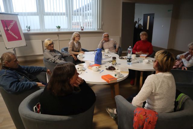 7 kobiet i 1 mężczyzna siedzą przy stołąch i rozmawiają