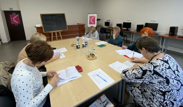 6 kobiet siedzi przy stołach i notuje na kartkach