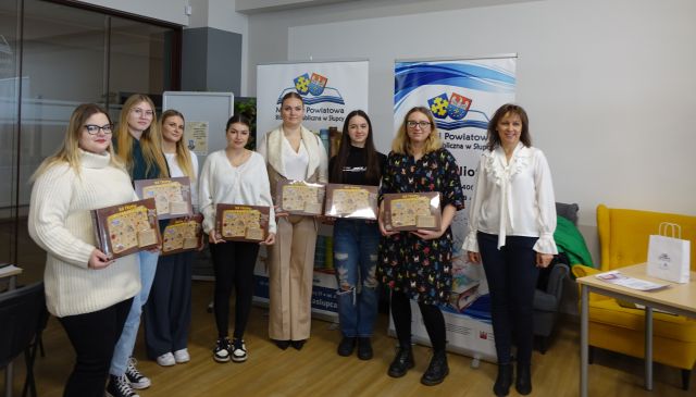 6 dziewczyn tworzących quest oraz graficzka i bibliotekarka pozują do zdjęcia z grami planszowymi