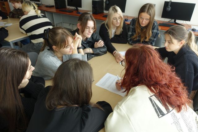 młodzież siedząca przy stołach rozwiązuje zadania