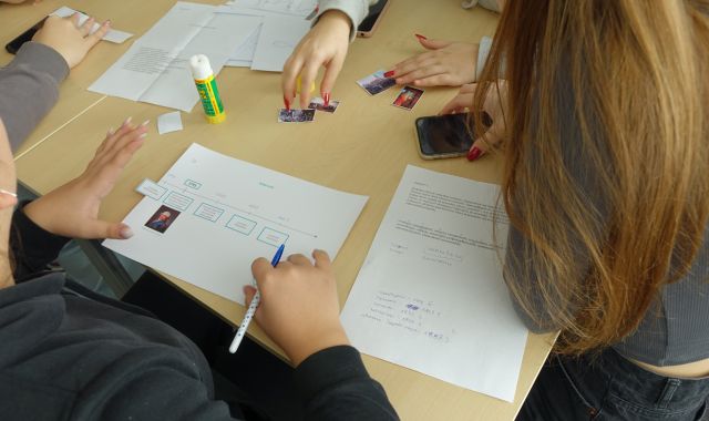 młodzież siedząca przy stołach rozwiązuje zadania