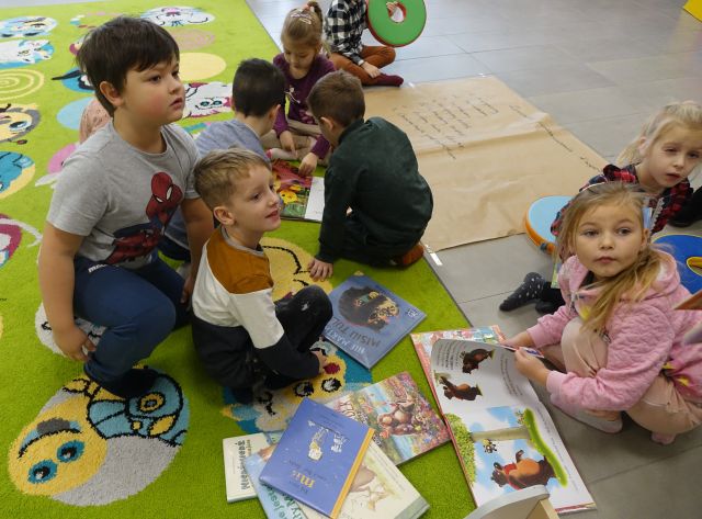 dzieci siedzą na kolorowym dywanie i przeglądają książki