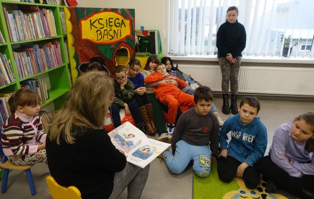 bibliotekarka czyte dzieciom siedzącym na kolorowym dywanie i pufach książkę