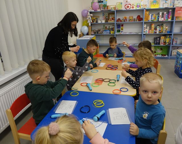 dzieci siedzą przy stołąch, na których leżą długopisy 3D oraz kolorowe filamenty